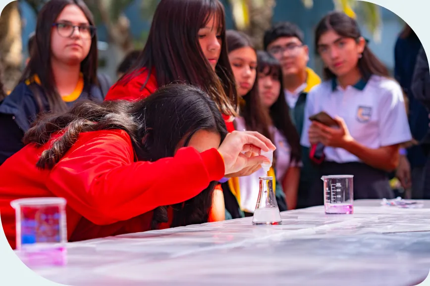 Estudiantes alrededor de una mesa de laboratorio mirando a una compañera mezclar una solución